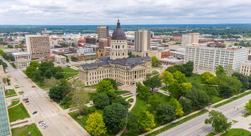 The Kansas state capitol building in bright daylight on a cloudless day with green grass and trees in the midst of losing their leaves