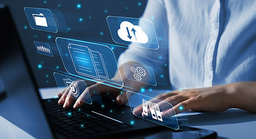 A person in a blue shirt works at a black laptop computer with various graphics layered overtop