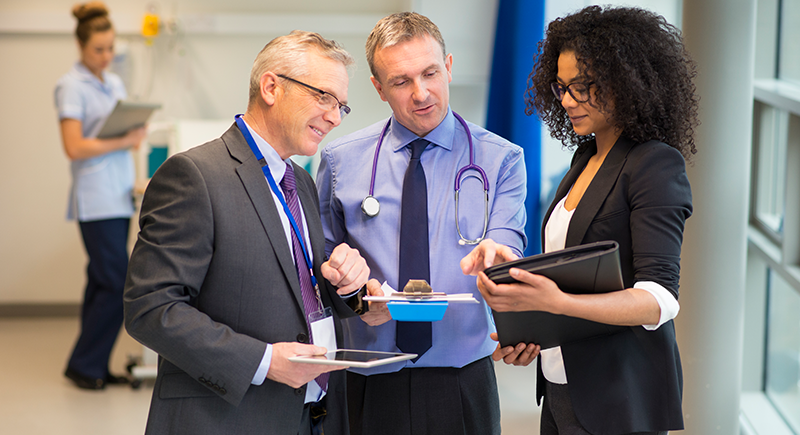 Medical professionals, two men and a woman, smile and look at clipboards in a hospital setting