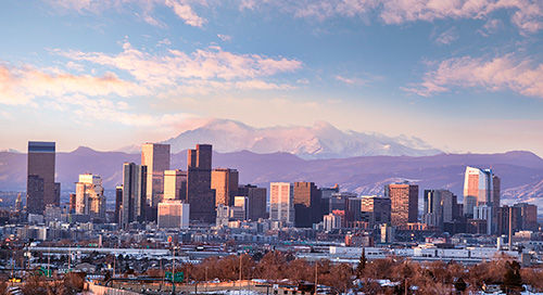 A panoramic shot of the Denver skyline with the Rocky Mountains in the background on a clear day