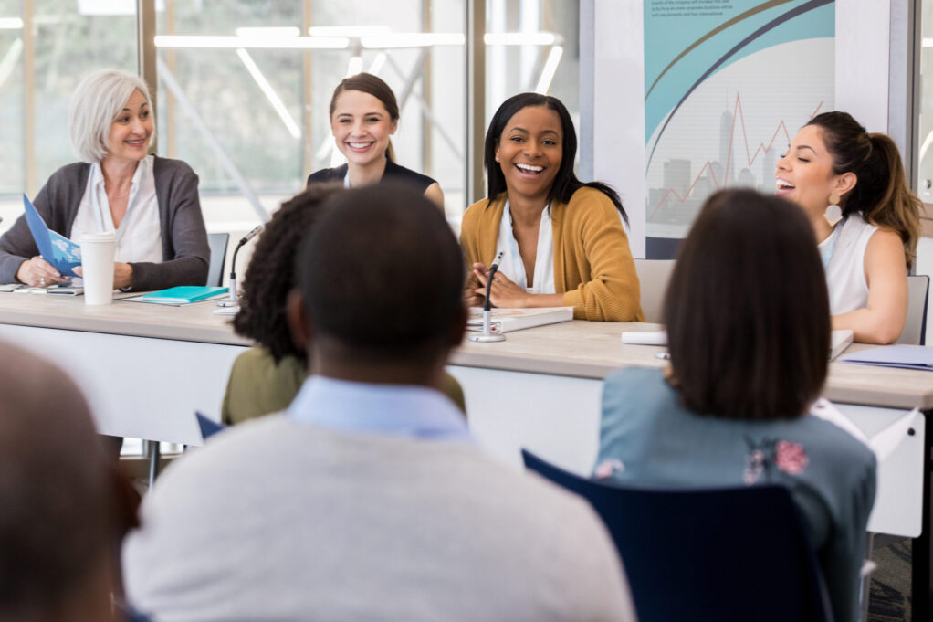 Diverse group of businesswomen give opinions and ideas during a panel discussion at a business conference.