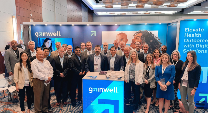 The Gainwell team stands next to each other smiling at the camera at a conference event with the blue Gainwell booth behind them.