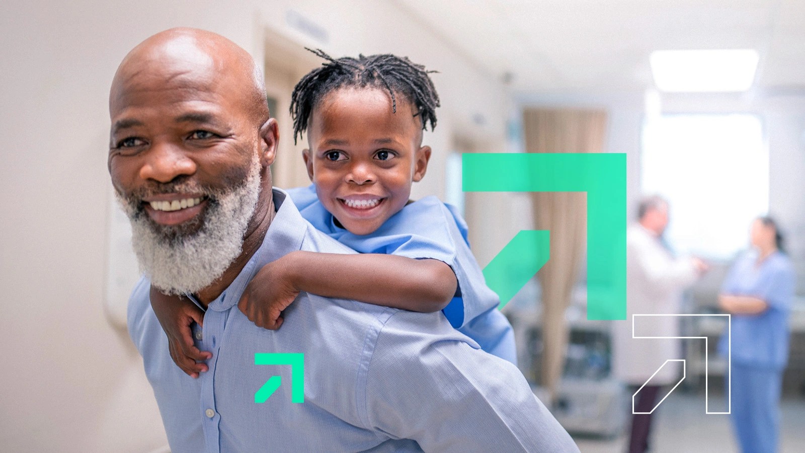 An African-American man with a white beard and blue shirt carries a young child in a medical gown smiling on his shoulders while a doctor and nurse are out of focus in the background