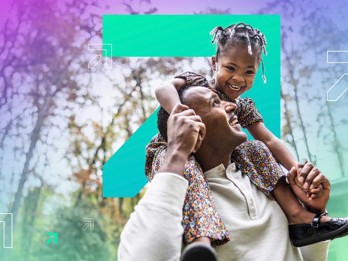 Close up of happy daughter on father’s shoulders as he holds her hands and looks up to her smiling.